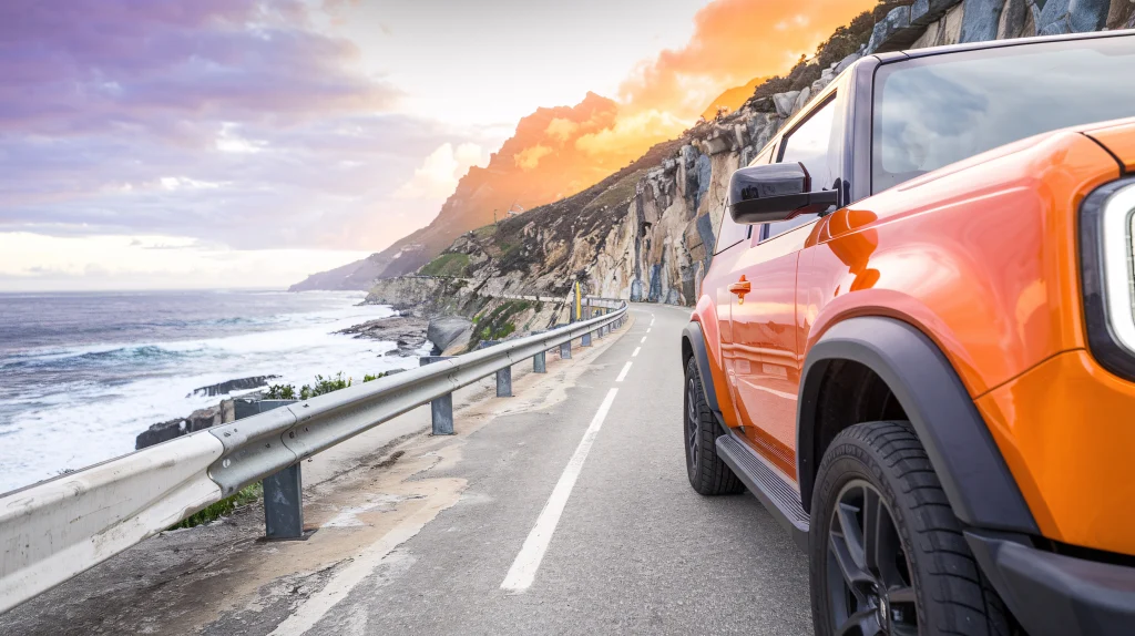 Car driving along a scenic ocean road, surrounded by blue waters and coastal cliffs.