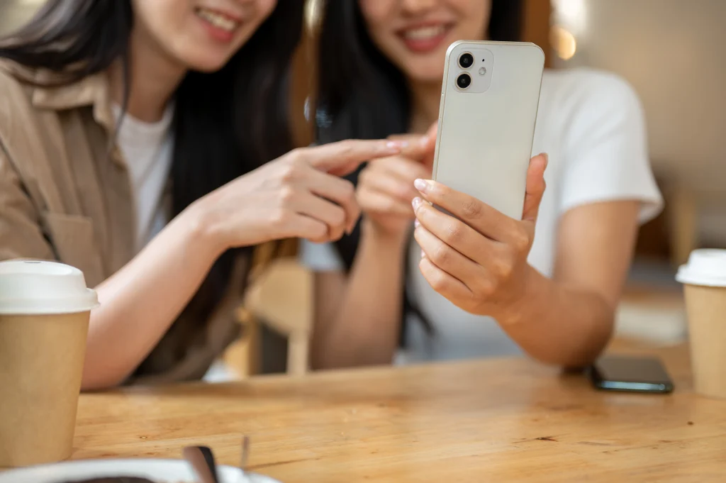 Two women look at Facebook videos on a mobile phone.